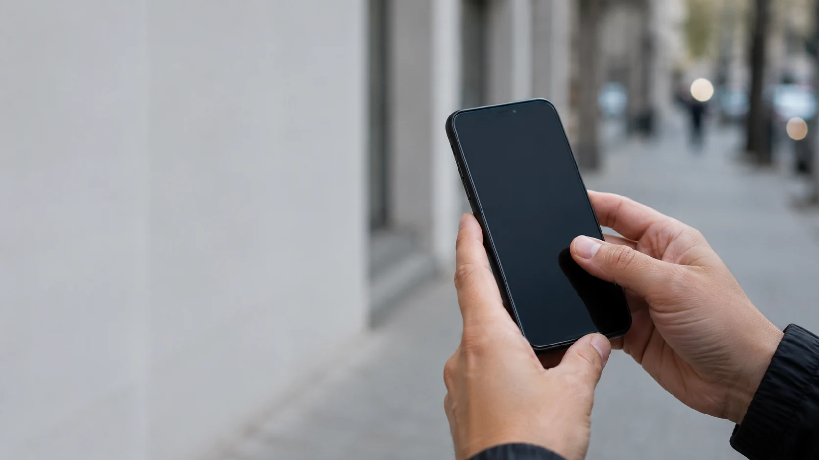 Manos sosteniendo un teléfono en la calle, frente a un consultorio, buscando un médico de la zona gracias al SEO para médicos